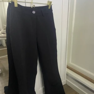 Svarta kostymbyxor med bootcut - Säljer ett par svarta kostymbyxor med bootcut passform. Byxorna har medel- låg midja, knapp och dragkedja framtill samt diskreta fickor bak. Perfekta för en stilren look.