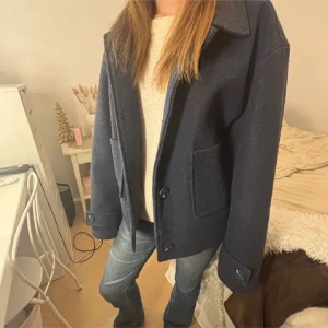 Mörkblå kappa - Säljer en mörkblå jacka  Jackan har knäppning med stora knappar och är lite boxig i modellen. Perfekt för dig som gillar en stilren och enkel look.