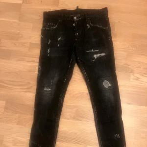 Svarta jeansbyxor från Dsquared2 ICON - Svarta jeansbyxor från Dsquared2 ICON med slitna detaljer och distressed look. Klassisk femficksmodell med knappgylf och silverfärgade nitar. Snyggt Dsquared2 ICON-läderpatch bak i midjan. Perfekta för en trendig streetstyle. Längd 102 cm Midja 50cm