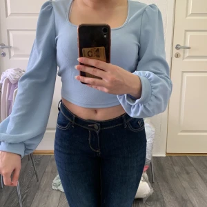 Ljusblå croppad topp med puffärmar från SHEIN - Säljer en ljusblå croppad topp från SHEIN med fyrkantig ringning och långa puffärmar. Toppen har en stilren design och är tillverkad i ett mjukt syntetmaterial. Perfekt för att lyfta din outfit med en trendig touch.