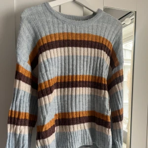 Randig ribbad stickad tröja i pastellblått från Ichi - Säljer en ribbad stickad tröja med breda ränder i pastellblått, senapsgult, brunt och beige från Ichi. Tröjan har rund halsringning och långa ärmar. Perfekt för dig som gillar färg och mönster! Väldigt snyggt med en vit underdel, typ en kjol eller linnebyxor. Skriv för fler bilder🩵