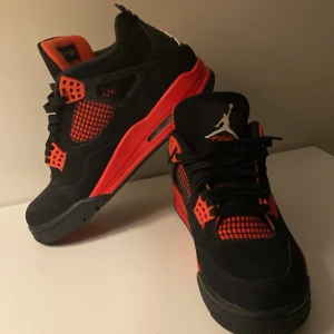 Nike Air Jordan 4 Retro Black/Red - Säljer ett par Nike Air Jordan 4 Retro i svart och rött. Skorna har klassisk siluett med svarta ovandelar i mocka, röda detaljer och meshpaneler. Ikonisk Jumpman-logga på plösen och hälen. Perfekta för dig som gillar streetwear och sneakerskultur.    Pris kan diskuteras vid snabb affär