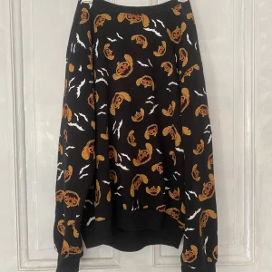 Svart Halloween-tröja med Stitch från Disney - Säljer en svart långärmad tröja från Disney med Stitch-motiv och pumpor i orange samt vita fladdermöss. Perfekt för Halloween! Tröjan är i bomull och polyesterblandning och har en avslappnad passform.