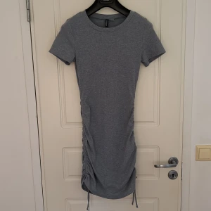 Fin Sommer klänning från H&M - Detta är en fin ljusgrå ribbad klänning med snören på sidan av klänningen, sitter jättefint och är fint till hela året!