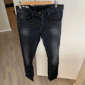 Svarta jeansbyxor från Dondup - Säljer ett par svarta jeans från Dondup med klassisk femficksdesign och smal passform. Jeansen har dragkedja och knapp i midjan samt diskreta slitningar för en snygg look. Perfekta till vardags och passar till det mesta. Använda 2 gånger. Perfekt skick.