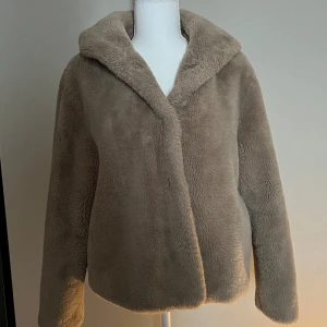 Beige pälsjacka med huva - Mysig beige pälsjacka med huva. Jackan har lång ärm.