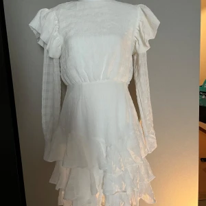 Vit volangklänning med långa ärmar - Säljer en romantisk vit klänning med långa ärmar och volangdetaljer. Klänningen är från boohoo