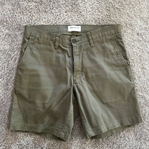 Olivgröna shorts från These Glory Days - Snygga olivgröna shorts från These Glory Days med klassisk passform. Shortsen har sidofickor, bakfickor med knapp och stängs med dragkedja och knapp framtill. Perfekta för varma dagar.