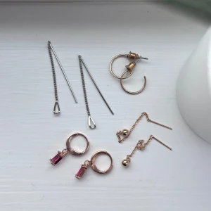 Fyra par örhängen i olika stilar - Säljer fyra par örhängen: ett par långa silverfärgade kedjeörhängen, ett par enkla guldfärgade hoops, ett par guldfärgade örhängen med rosa hängande sten och ett par små guldfärgade örhängen med kula och kedja. Skickas i en liten praktisk plastförpackning 🩷 
