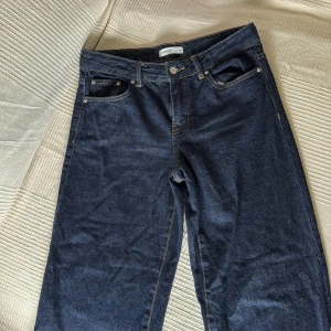 Mörkblå raka jeans - Säljer ett par mörkblå jeans med raka ben och klassisk femficksdesign. Jeansen har normal passform och är tillverkade i denim med synliga kontrastsömmar. Perfekta för en avslappnad stil.