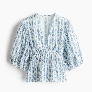 Vit och blå blus ifrån hm - Säljer en vit blus med blått mönster och djup v-ringning. Blusen har puffiga trekvartsärmar och smockad midja som ger en snygg passform🫶🏻 Helt slutsåld och ny med prislapp