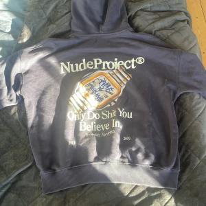 Mörkblå hoodie från Nude Project - Säljer en mörkblå hoodie från Nude Project i storlek L men passar M. Tröjan har tryck både fram och bak med text och en klockgrafik på ryggen. Klassisk huva och magficka. Perfekt för dig en sommarkväll. Nypris 1700 kr - mitt pris 450 💸