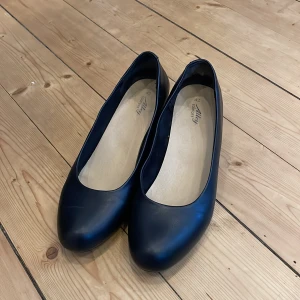 Svarta ballerinaskor med låg klack  - Stilrena svarta ballerinaskor från Alley med rund tå och låg klack. Skorna har en klassisk design i syntetmaterial och passar perfekt till många olika outfits. Enkla att ta på och av, och ger en tidlös look.