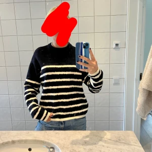 Mörkblå och vit randig stickad tröja - Säljer en mörkblå stickad tröja med vita ränder. Tröjan har lång ärm, rund halsringning och en avslappnad passform. 