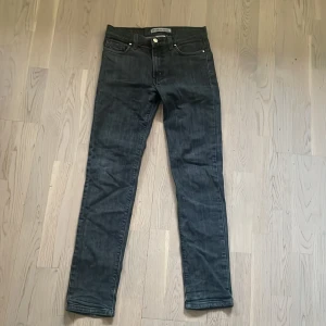 Svarta jeansbyxor från Woodbird Denim - Säljer ett par svarta jeansbyxor från J.lindeberg.  Med dragkedja och knapp framtill. Jeansen har en slim passform och raka ben. Perfekta till dig som gillar stilrena och enkla jeans.