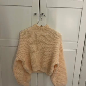 Beige stickad croppad tröja - Mysig beige stickad tröja med hög hals och croppad passform. Tröjan har långa ärmar och breda muddar vid ärmslut och nederkant. Perfekt för lager-på-lager under kyliga dagar. Aldrig använd 