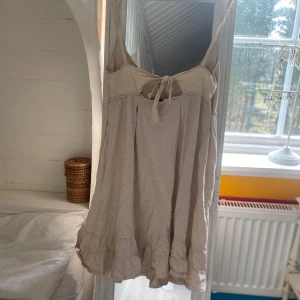 Beige kortklänning med volang från Cubus - Supersöt beige kortklänning från Cubus med smala axelband och volang nertill. Klänningen har knytning framtill och är perfekt för varma dagar. Lätt och luftig modell som ger en avslappnad känsla.