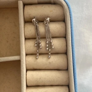 Silverfärgade örhängen med kedjor - Säljer ett par snygga silverfärgade örhängen med flera tunna kedjor som hänger ner och små kulor längst ut. Perfekta för att ge en cool touch till din outfit!
