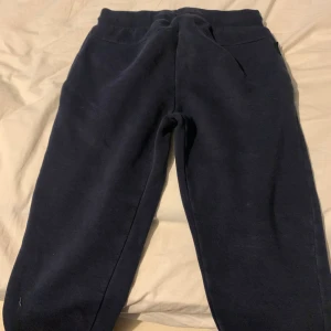 Mörkblå mjukisbyxor från Peak Performance - Mörkblå mjukisbyxor från Peak Performance med resår och snörning i midjan. Byxorna har två sidofickor och är tillverkade i ett mjukt material som passar perfekt för avslappnade dagar eller träning. Storleken är 150 men det gick inte att välja i menyn.