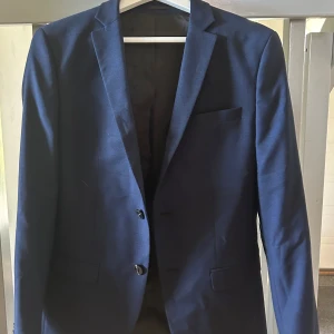 Mörkblå kostym  - Säljer en stilren superfin mörkblå kostym från Jack & Jones i super slim passform. Kostymen består av kavaj med två knappar och matchande byxor med knappdetalj bak.