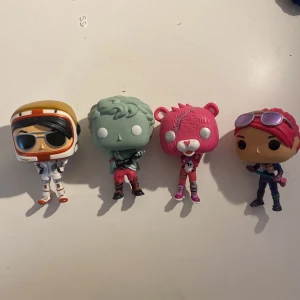 Fyra Fortnite Funko Pop! figurer - Säljer fyra Fortnite Funko Pop! figurer: en astronaut i vit och orange dräkt, en grönhårig zombie, en rosa björn och en figur med rosa hår och lila kläder. Perfekta för samlare eller Fortnite-fans!
