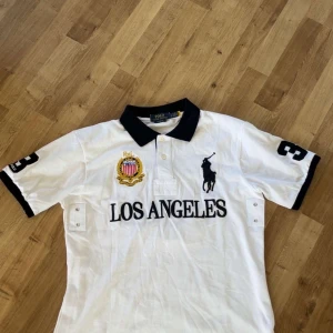 Vit piké från Polo Ralph Lauren  - Säljer en fet polo Ralph lauren piké som har Los Angeles. Tröjan är perfekt inför sommaren 🏝️🌊☀️🏖️ och även nu på våren tröjan är även i storlek L och är nästan Helt ny och har därför inga skador. Skriv vid frågor ☺️