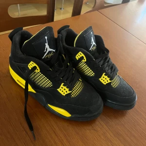 Svarta och gula Nike Air Jordans 4 - Säljer ett par svarta och gula Nike Air Jordans med klassisk Jumpman-logga på plösen och sulan. Skorna har snörning, meshdetaljer på sidorna och platt sula. Perfekta för dig som vill sticka ut med en färgstark sneaker.