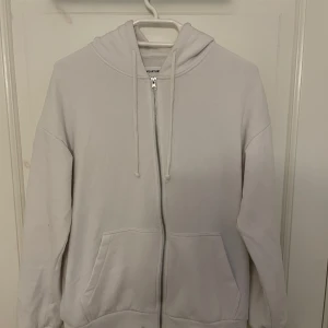 Vit hoodie med dragkedja från YOURTURN - Säljer en enkel vit hoodie från YOURTURN med dragkedja framtill och två fickor. Tröjan har huva med dragsko och långa ärmar. Perfekt för en avslappnad stil. Fläck på sista bilden 