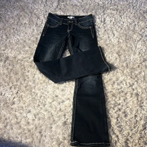Blå jeansmed broderade bakfickor från Gina Tricot - Säljer ett par blå jeansbyxor från Gina Tricot med vita kontrastsömmar och snygga broderade detaljer på bakfickorna. Byxorna har bootcut-modell och klassisk femficksdesign. 