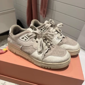 Beige sneakers från Acne Studios - Snygga beige sneakers från Acne Studios med vit och ljusgrå detalj. Skorna har snörning, rund tå och platt sula. Perfekta för dig som gillar stilrena och trendiga skor med diskret logga på hälen och innersulan. Liten fläck som syns på bilden men går nog att få bort! 