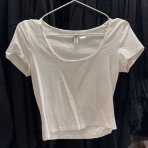 Vit croppad t-shirt från H&M - En enkel och stilren vit croppad t-shirt från H&M med rund halsringning och korta ärmar. Perfekt att matcha med jeans eller kjol för en avslappnad look.