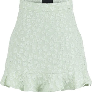 Grön blommig kjol från Pieces - Superfin mintgrön kortkjol från Pieces med broderade blommor och volangkant nertill. Kjolen har en lätt A-linjeform och är perfekt för dig som vill ha en söt och trendig look. Materialet känns mjukt och har en lätt struktur.