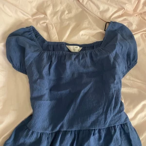 Blå blus från H&M - Supersöt blå blus från H&M med puffärmar och fyrkantig ringning. blusen har en lätt rynkad struktur och är perfekt för varma dagar. 