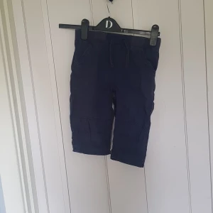 Mörkblå byxor från Lindex Kids - Mörkblå byxor från Lindex Kids med dragsko i midjan och mjuk resår. Byxorna har fickor fram och bak samt förstärkta knän. Perfekta för lek och vardag, tillverkade i bomull för skön känsla.