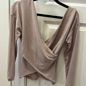 Beige/rosa  omlottopp från NLY Trend - Supersnygg beige omlottopp från NLY Trend med ribbad struktur och djup v-ringning. Långärmad modell i mjukt material som sitter skönt och ger en trendig look. Perfekt att styla med jeans eller kjol för en cool vibe.