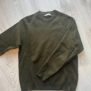 Olivgrön stickad tröja från Zara - Snygg olivgrön stickad tröja från Zara i klassisk modell med rund halsringning och ribbade muddar. Perfekt för lager-på-lager och passar till både jeans och kjol. Enkel och stilren design som funkar året runt.