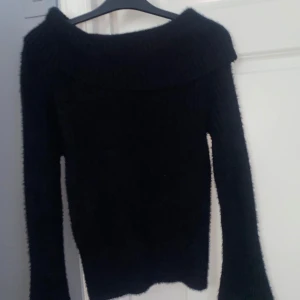 Svart stickad offshoulder-tröja - Mysig svart stickad tröja med bred offshoulder-krage och lång ärm. Perfekt för dig som gillar en enkel men ändå snygg look. Tröjan har en fluffig känsla och sitter skönt på kroppen. Passar till jeans eller kjol för en chill vibe.