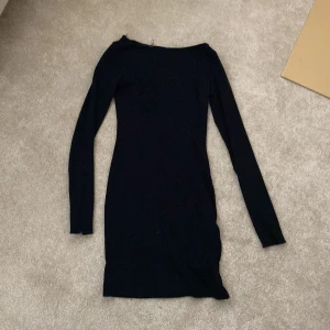 Svart långärmad klänning från Bershka - En svart, tight, ribbad och enkel långärmad klänning från Bershka. Modellen är kort och har en rak, stilren passform med rundad halsringning. Perfekt basplagg som funkar till många olika looks.