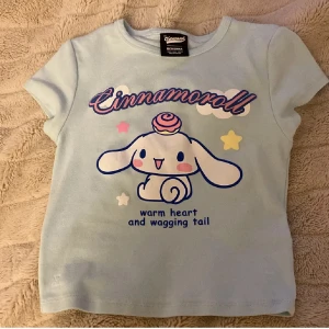 Cinnamoroll t-shirt från Bershka - Söt ljusblå t-shirt från Bershka med Cinnamoroll-tryck och texten 'warm heart and wagging tail' framtill. Kortärmad modell i mjuk bomull, perfekt för dig som gillar kawaii-stil och pastellfärger. Motiv med stjärnor och gullig tecknad figur. I storlek M men sitter som en S 
