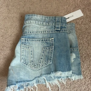Lågmidjade jeansshorts från Gina Tricot - Helt nya med prislapp på helt slutsålda på hemsidan. Säljer ett par ljusblå lågmidjade jeansshorts från Gina Tricot. De har slitna detaljer, fransig rå kant nertill och klassiska fickor både fram och bak. Perfekta för sommaren och ger en avslappnad vibe.