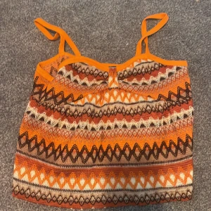 Mönstrad stickad linne-topp från SHEIN - Färgglad stickad linne-topp från SHEIN med smala axelband. Toppen har ett coolt mönster i orange, brunt, beige och vitt med olika geometriska former. Perfekt för dig som gillar boho-vibes och vill sticka ut med färg och mönster.
