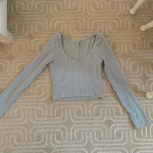 Ljusblå croppad stickad tröja - Ljusblå stickad tröja med kabelstickat mönster och croppad passform. Lite uttöjd i ena ärmen men i bra skick i övrigt.