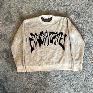 Grå stickad tröja från Weekday - Säljer en gråmelerad stickad tröja från Weekday i storlek S. Tröjan har svart grafiskt tryck framtill, ribbade muddar och rund hals. Perfekt för dig som gillar streetstyle och vill ha något unikt i garderoben.