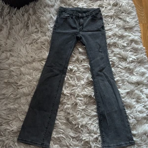 Grå bootcut jeans med slitning - Snygga grå jeans med bootcut passform och låg midja. Jeansen har en cool sliten detalj på ena låret och klassiska fem fickor. 