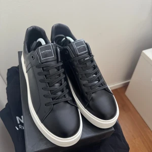 Balmain sneakers - Stilrena svarta sneakers från Balmain i skinn med vit, chunky sula och tydlig Balmain-logga under och bak på sulan. Klassisk låg modell med rund tå och svarta skosnören. Perfekta för dig som vill ha en clean och lyxig look.