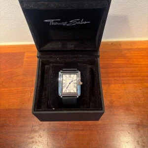 Klassisk Quartz klocka med svart armband - Stilren klocka från med rektangulärt silverfärgat boett, vit urtavla med romerska siffror och svarta visare. Svart läderarmband ger en tidlös look. Perfekt accessoar för dig som gillar klassisk och elegant stil. Perfekt för sommaren. Klocklåda ej inkluderad