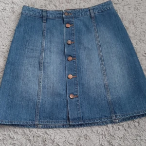 Jeanskjol med knappar från L.O.G.G. - Snygg blå jeanskjol från L.O.G.G. i A-linjeformad modell. Kjolen har knappar framtill, bälteshällor och klassisk denimlook. Perfekt till sneakers eller boots för en chill stil.