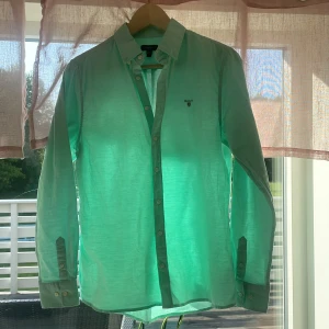 Ljusgrön skjorta från GANT 170 cm - Snygg ljusgrön skjorta från GANT med klassisk krage och knappar hela vägen. Skjortan har lång ärm och diskret broderad GANT-logga på bröstet. Perfekt för dig som gillar stilrena och fräscha plagg.