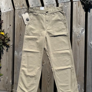 Beiga Carhartt cargopants wide fit - Snygga beiga cargopants från Carhartt med raka, vida ben och stora fickor framtill. Byxorna har klassisk logga på bakfickan och är gjorda i slitstark bomull. Perfekta för en avslappnad streetstil med touch av vintage. Helt oanvända.     L: 30/31 W:31 