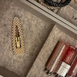 Mix av guldiga smycken med pärldetaljer - Säljer ett set med smycken: en hårklämma i guld med vita pärlor, en stor guldig brosch i form av en blomma med pärla i mitten samt två guldiga armband, varav ett har hamrad yta. Perfekt för dig som gillar vintagevibbar och unika accessoarer.